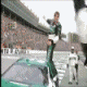 Animated contact sheet showing a person in green racing suit performing acrobatic flips on a race track with cars and spectators in background.