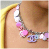 A person wearing a yellow garment and a pink-and-white beaded necklace with a purple interlocking-C pendant, with vertical "CHANEL" text on the left edge.