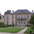A static pixelated image of a large two-story house with a dark roof, multiple windows, and a pathway leading to the entrance, surrounded by greenery.