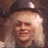 Pixelated static image of a person with light-colored hair wearing dark clothing and a cap, set against a brown background.