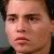 Pixelated close-up of a person's face with neutral expression, dark hair, and light skin tone against a blurred background.