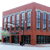 Pixelated image of a red building with large windows and dark ground-floor openings, set against a light background.