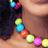 A pixelated image shows a person's neck and shoulder with a colorful beaded necklace, alongside bright cyan background text in pink block letters.