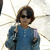 Pixelated static image of a person in blue clothing holding an object with purple accents against a bright background with radiating lines.