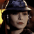 Static pixelated image of a person wearing a dark blue cap with light trim, visible facial features including eyes and lips, and partial hair or clothing details against a dark background with yellow lighting elements.
