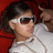 Pixelated image of a person with dark hair wearing white-framed sunglasses and a light-colored shirt against a red background.