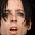 Pixelated close-up of a person's face with light skin tone, dark hair, and mouth open in a neutral expression against a dark background.