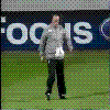 A man in a gray jacket and black pants performs soccer ball tricks on a green field with a blue 'FOCUS' banner background.