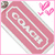 A pink Coach logo tag with white text and border, surrounded by a light pink frame. The background contains pixelated patterns including green, blue, orange, and red shapes.