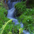 Pixelated green and blue landscape with indistinct shapes resembling foliage and water, rendered in low-resolution mosaic style.
