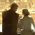 Two pixelated figures in dark clothing stand side-by-side against a light brown background with visible dithering and low-resolution rendering artifacts.