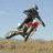 A pixelated image shows a person riding a dirt bike on a sandy terrain with blue sky background, accompanied by text elements.