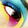 A close-up of a human eye with vibrant, multicolored eyeshadow in blue, yellow, and pink hues, featuring a white highlight on the iris.