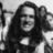 Black-and-white pixelated image of a person with long dark hair wearing a high-collared garment, set against a light background.