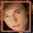 A static image of a person with light brown hair and blue eyes, wearing dark clothing against a dark background. The face is framed by three distinct border colors: red-brown, white, and gray-blue.