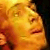 Pixelated close-up of a person's face with closed eyes, warm orange and yellow tones dominating the image, dark background on the right side.