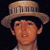 Pixelated image of a person wearing a wide-brimmed straw hat with vertical slats, dark hair visible beneath the hat, and a light-colored shirt against a dark background.