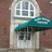 Static image of a building facade with a white-framed window above a teal awning and dark door, set against a brown background.