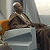 Pixelated static image of a humanoid figure in armor seated on a chair with an orange armrest, set against a muted background.