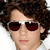 A person with curly brown hair and dark red sunglasses appears in a of four , showing slight variations in facial expression across the sequence