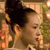 Pixelated close-up of a person with dark hair tied up, wearing a light-colored top, against a blurred background with warm tones.