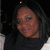 Pixelated close-up of a person with dark hair and light skin, wearing dark clothing against a dark background.