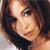 Pixelated close-up of a person with brown hair and light skin, wearing a dark top, against a light background.