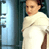 Pixelated static image of a person in white clothing standing near a blue-tinted window or screen with dark background elements.