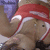 A person in a red and white headband with visible chest, arms raised, and purple background elements.