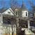 Pixelated image of a multi-story building with a sloped roof, small windows, and a tower-like structure under a blue sky.