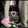 A grayscale image of two people's legs and feet with one person wearing pink sneakers and a pink heart symbol overlaid on the lower center.