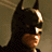 Batman character in dark cowl with pointed ears, bat symbol on chest, and red background elements.