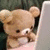 Animated brown teddy bear with white snout and paws, holding a pink object against dark green background.