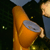 A pixelated orange cone-shaped object with a gray circular top is held by a hand against a dark background with green and yellow speckles.