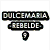Pixelated image with text 'DULCEMARA REBELDE' and lightbulb icon above group photo of people, red-haired woman in black top, and person holding game controller.