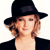 Pixelated image of a person with light brown curly hair wearing a black wide-brimmed hat and black clothing against a white background.