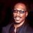Static pixelated image of a bald man with dark sunglasses wearing a dark shirt against a black background.