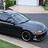 Pixelated static image of a silver sedan parked on a paved surface with green grass and trees in the background.