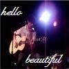 A pixelated image shows a person playing an acoustic guitar under a bright stage light, with 'hello' text in the top left and 'beautiful' text in the bottom right.
