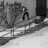 Black-and-white animation of a figure in dark pants and light top performing a jump over a railing, with trees and building background.