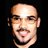 Pixelated static image of a bald man's face with light skin, dark eyebrows, and a mustache against black background.