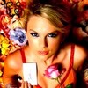A woman with blonde hair in a red halter top holds a white card with a blue and purple flower, surrounded by colorful floral patterns.