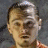 Pixelated close-up of a person's face with light brown hair, neutral expression, and visible ear against a dark gray background.