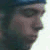 Pixelated close-up of a person's face in profile view, showing dark hair and a neutral expression against a blurred background.