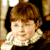 Static pixelated image of a person with brown hair and white ruffled collar against dark background.