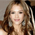 A static pixelated image of a person with long brown hair, closed eyes, and a slight smile, wearing a light-colored top against a neutral background.