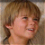 Pixelated close-up of a person's face with light brown hair and visible facial features including eyes, nose, mouth, and ear.