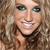 A pixelated close-up of a person with light brown hair, blue eyes, and a broad smile showing teeth, wearing a dark choker necklace against a blurred background.