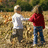 Two children holding hands in a grassy field, one in white shirt and gray pants, the other in red hoodie and blue jeans; orange text on black background reads "you can still love on".