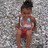 Pixelated image of a person in a bikini top and red bottoms standing against a textured gray background.
